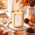 Load image into Gallery viewer, A gold metal candle jar with two lit wicks sitting on a round marble platform in a decorated Autumn scene. The label reads TABOR OLIVE Premium Coconut Wax Candle