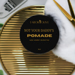 Load image into Gallery viewer, Black jar flat lay on gold surface next to white towel and gold scissors. The blackjar has gold text that says, "not your Daddys pomade. Water Soluble. Alcohol free."