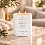 Load image into Gallery viewer, A white double-wick coconut wax candle by Tabor Olive sits on a marble surface in a softly lit, cozy interior setting with a knit blanket, greenery, and blurred home decor in the background.