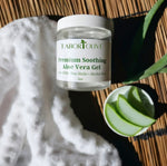 Load image into Gallery viewer, Clear jar with white lid laying on bamboo next to cut pieces of aloe plant, white towel and green text that says, "premium Soothing aloe vera gel. Non- GMO non-sticky alcohol free."