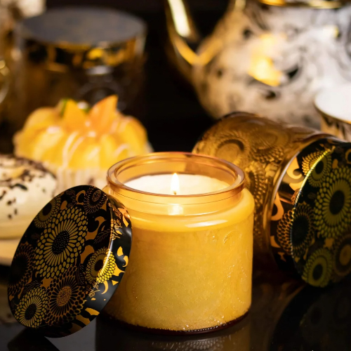 Gold candle burning next to black and gold candle lid surrounded by flowering branches.