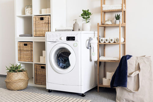 A washing machine surrounded by soft, natural linens, wicker baskets, and bamboo racks