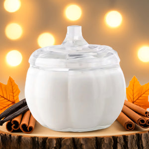 Pumpkin candle jar with a lid on a wooden surface with cinnamon sticks and vanilla beans, blurred lights in the background.
