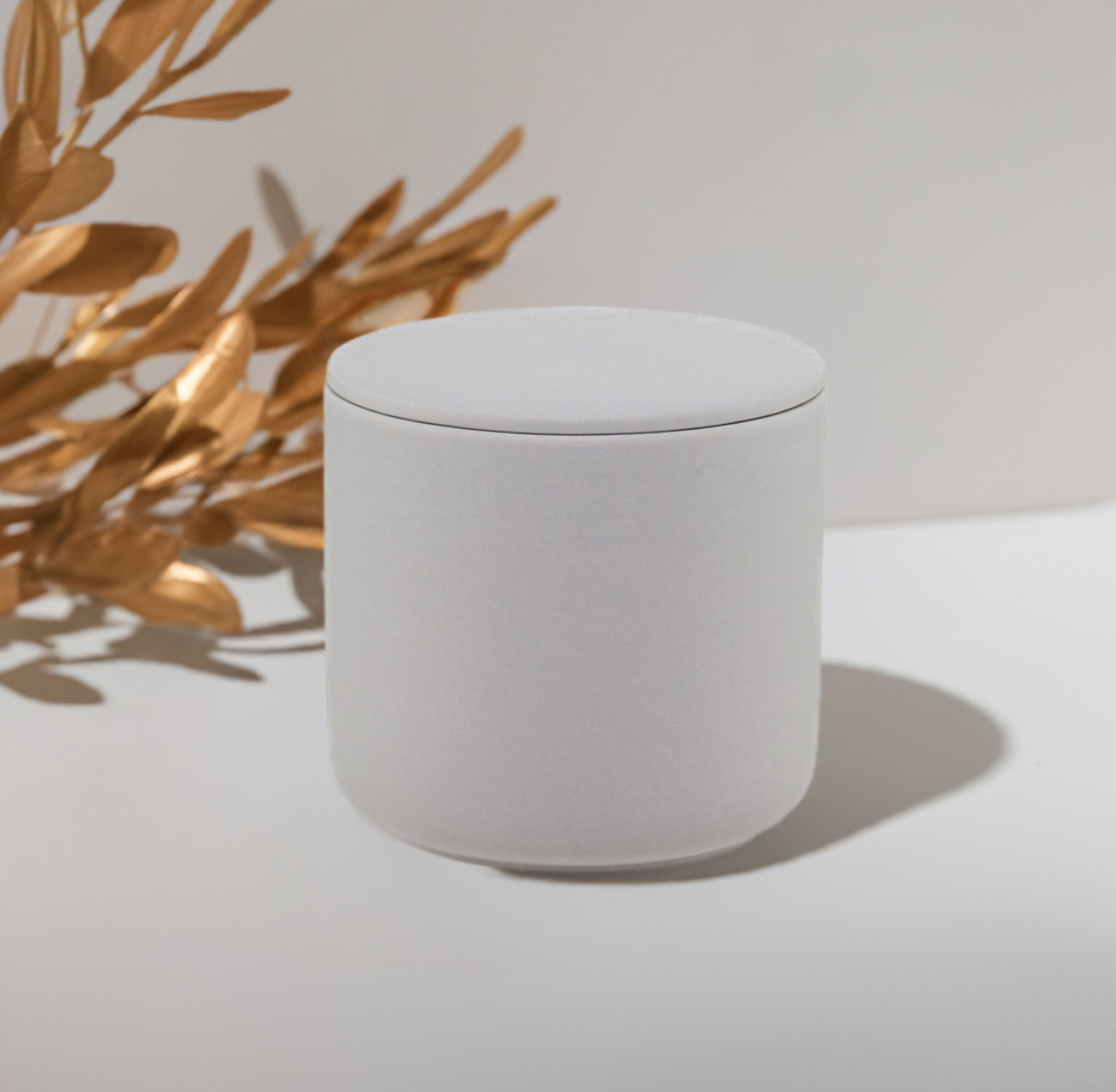 Gray ceramic candle sitting on a whiye platform next to gold flowering branches.