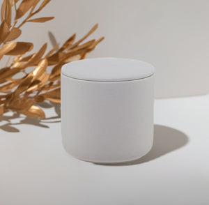 Gray ceramic candle sitting on a whiye platform next to gold flowering branches.