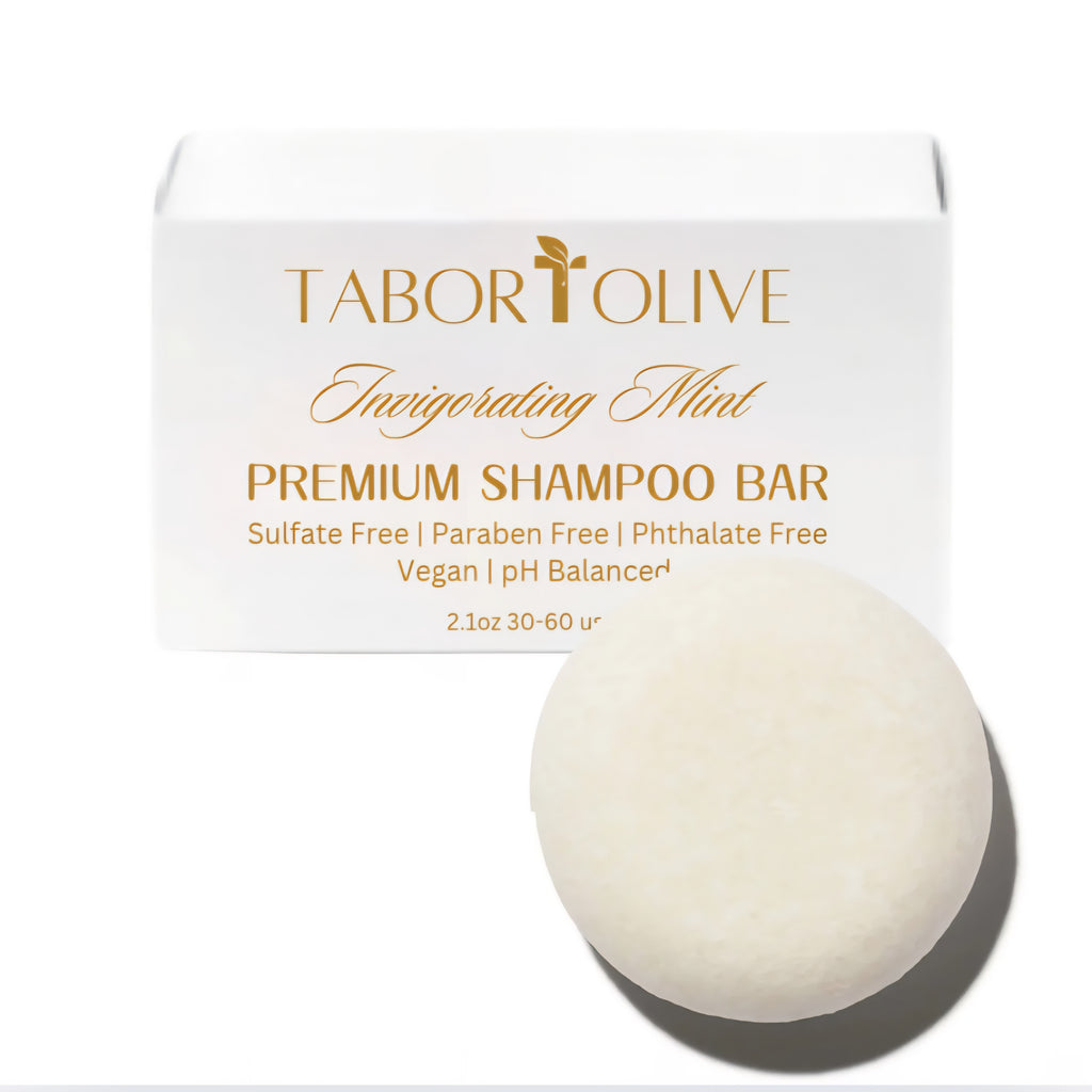 White soap box next to round shampoo bar with gold text that says, "invigorating mint shampoo bar. Sulfate free, paraben free, phthalate free, vegan, ph balanced"