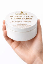 Load image into Gallery viewer, Hand holding a container of Tabor Olive Glowing Skin Sugar Scrub on a white background
