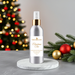 Load image into Gallery viewer, Silver room spray bottle with gold cap on a marble stand, Christmas tree and decorations in the background

