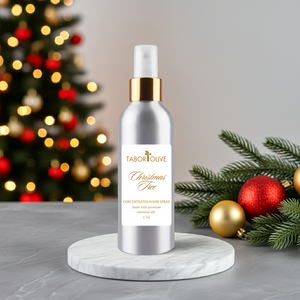 Silver room spray bottle with gold cap on a marble stand, Christmas tree and decorations in the background