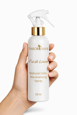 Load image into Gallery viewer, Hand holding a Tabor Olive Fresh Linen natural odor neutralizing spray bottle against a white background
