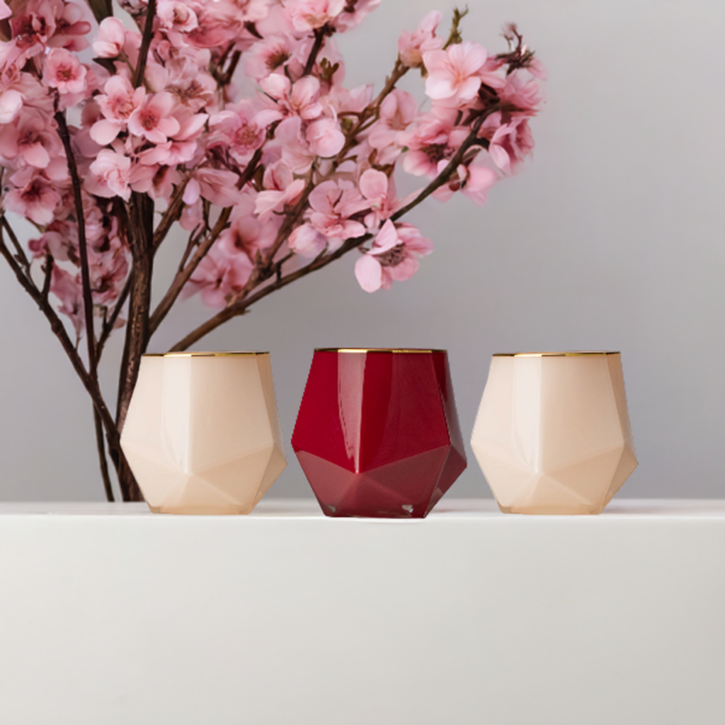 Pink and red gold candles on white surface with cherry blossom flowering branches in the background. 