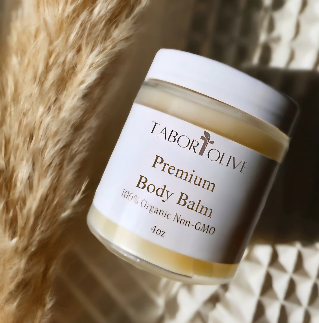 Premium body balm in a glass jar laying on linens next to pampas grass.